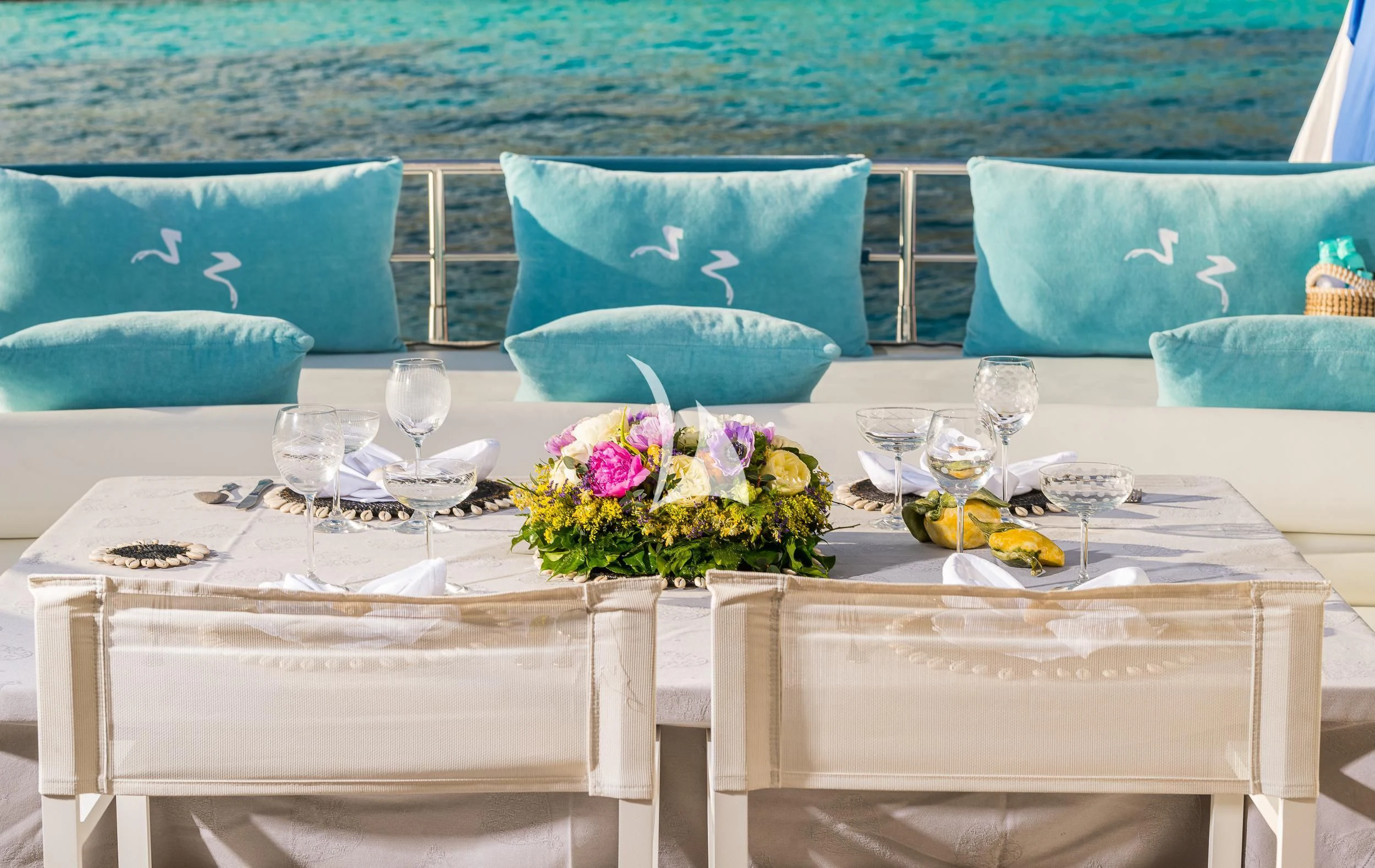 a table set with flowers and a blue couch and a large body of water in the background aboard FROGGY Yacht for Sale