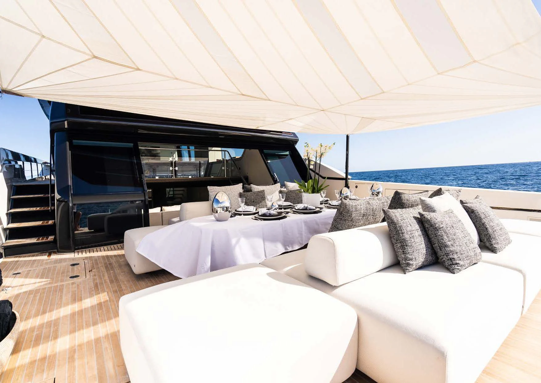 a large white lounge chair next to a large white bed with a large white and black striped pillow aboard ANMAX Yacht for Sale