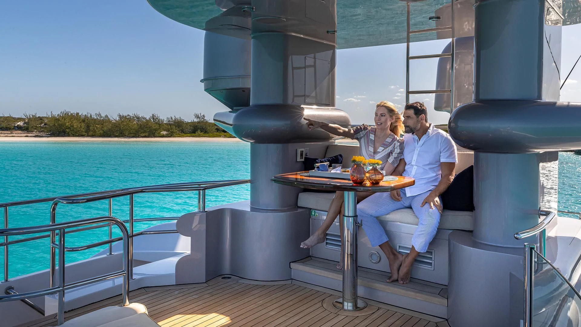 a man and woman sitting at a table with a drink and a large body of water in the aboard STARSHIP Yacht for Charter