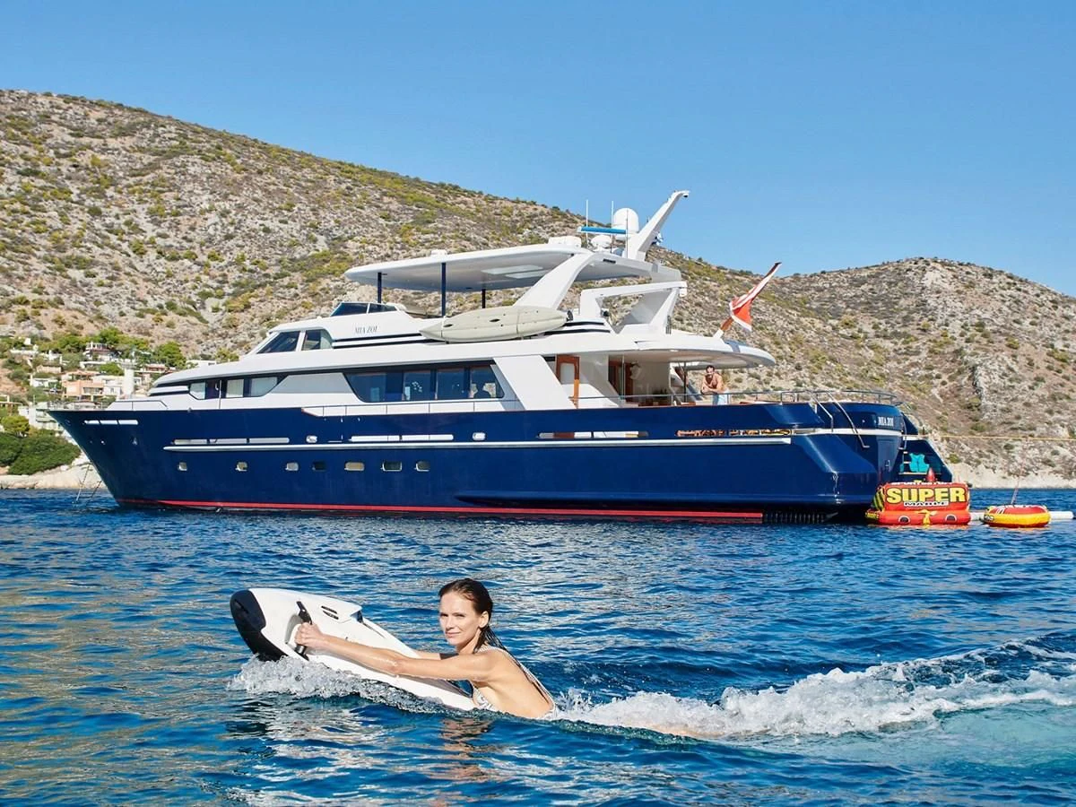 a person on a surfboard in the water next to a boat aboard MIA ZOI Yacht for Charter