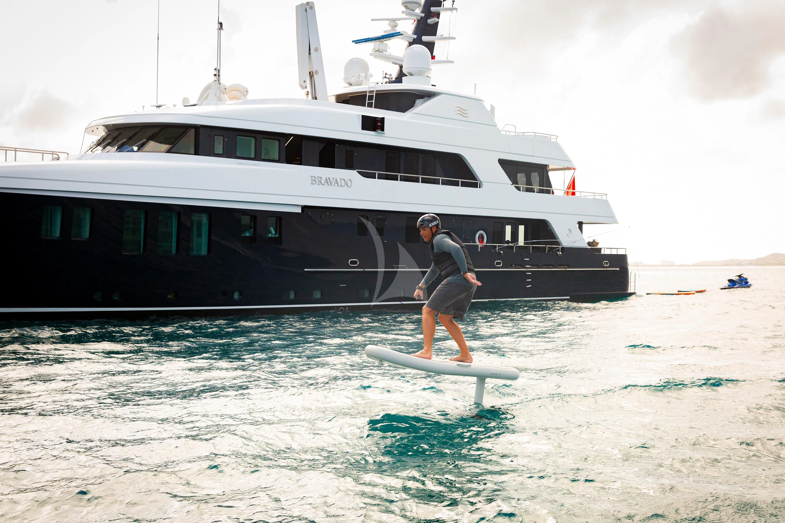 a man on a surfboard in front of a boat aboard BRAVADO Yacht for Sale