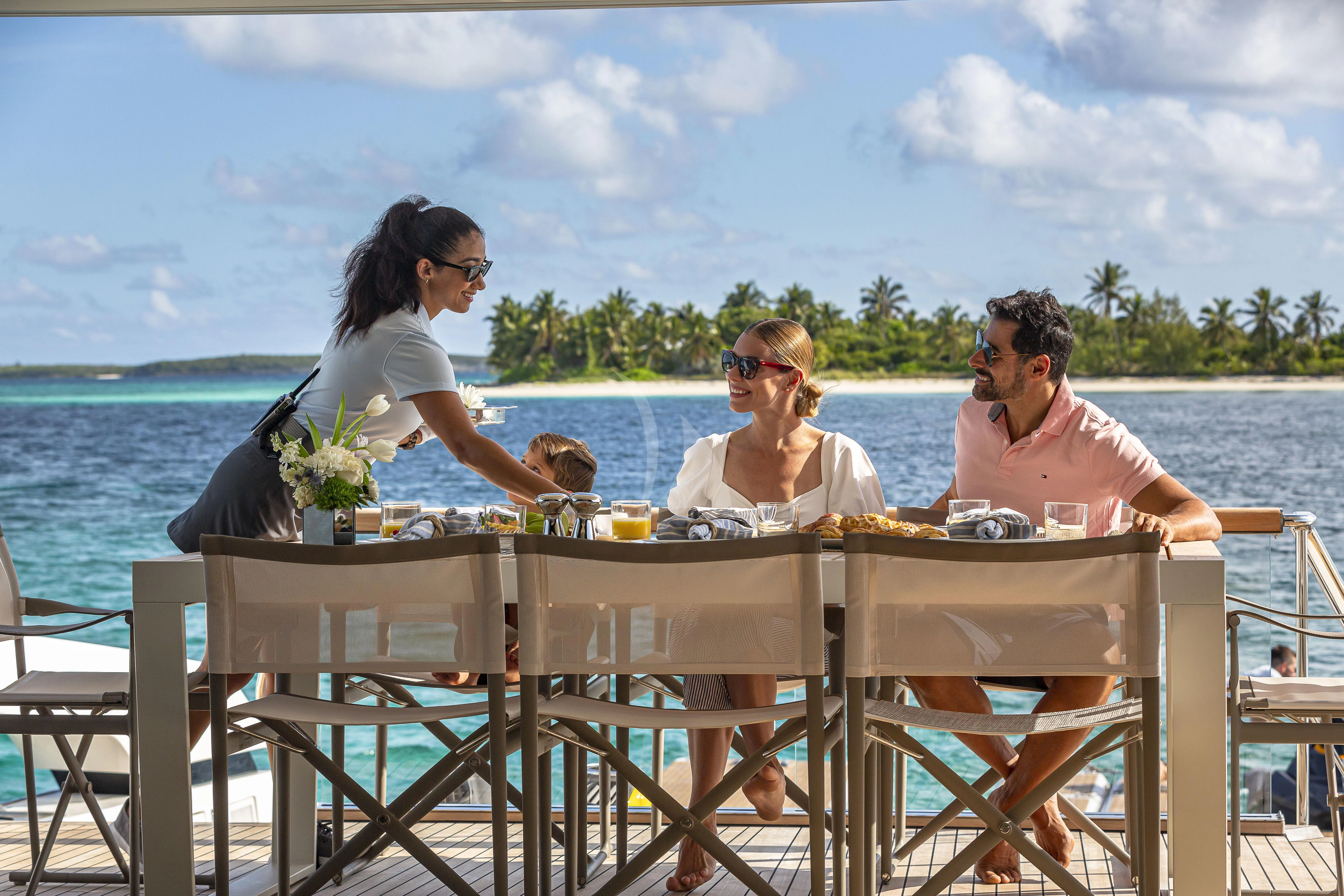 a group of people sitting at a table with flowers in front of a body of water aboard NO MATTER WHAT Yacht for Charter