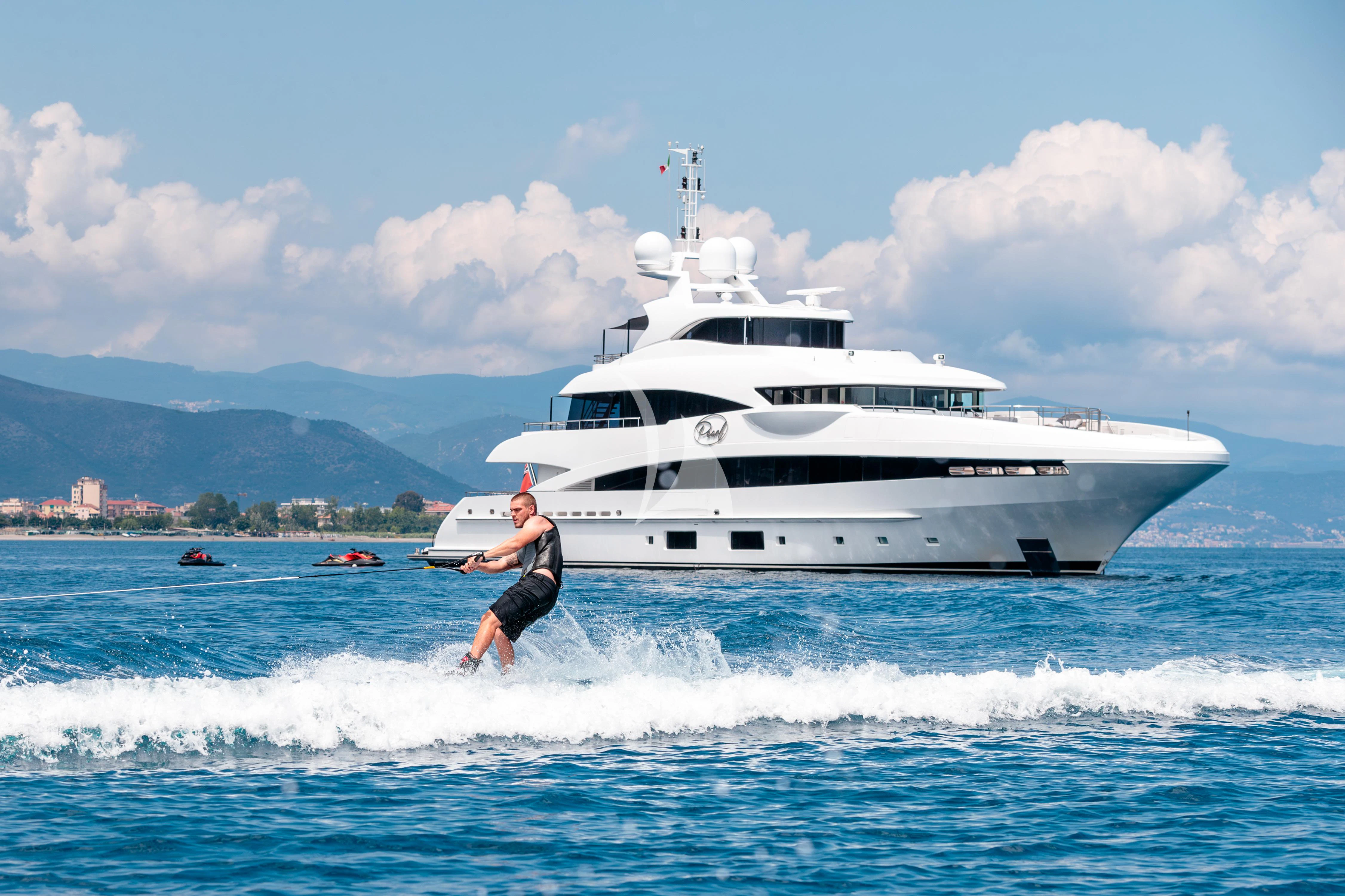 a man on a surfboard in the water next to a white boat aboard PEARL Yacht for Sale