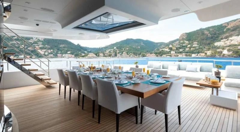 a room with a table chairs and a large building with a view of mountains and water aboard PEARL Yacht for Sale