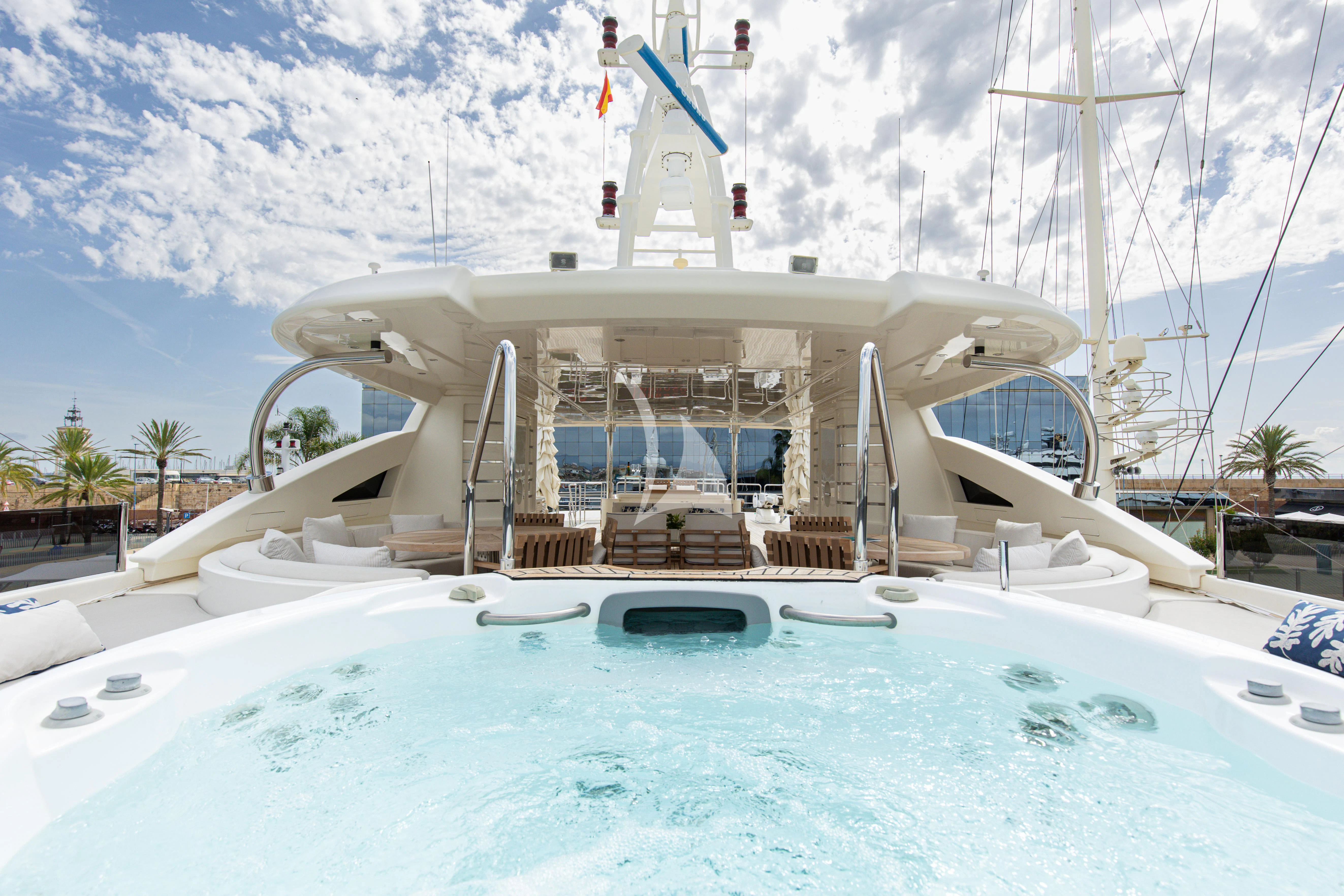 a swimming pool with a white building and blue sky and clouds aboard PALATIAL Yacht for Sale