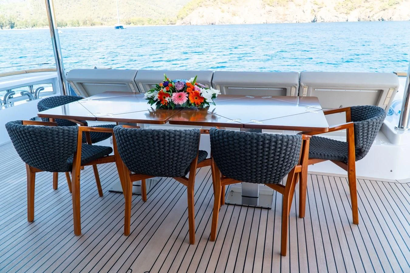 a table set with chairs and flowers on a deck with a body of water in the background aboard SHELLS X Yacht for Sale