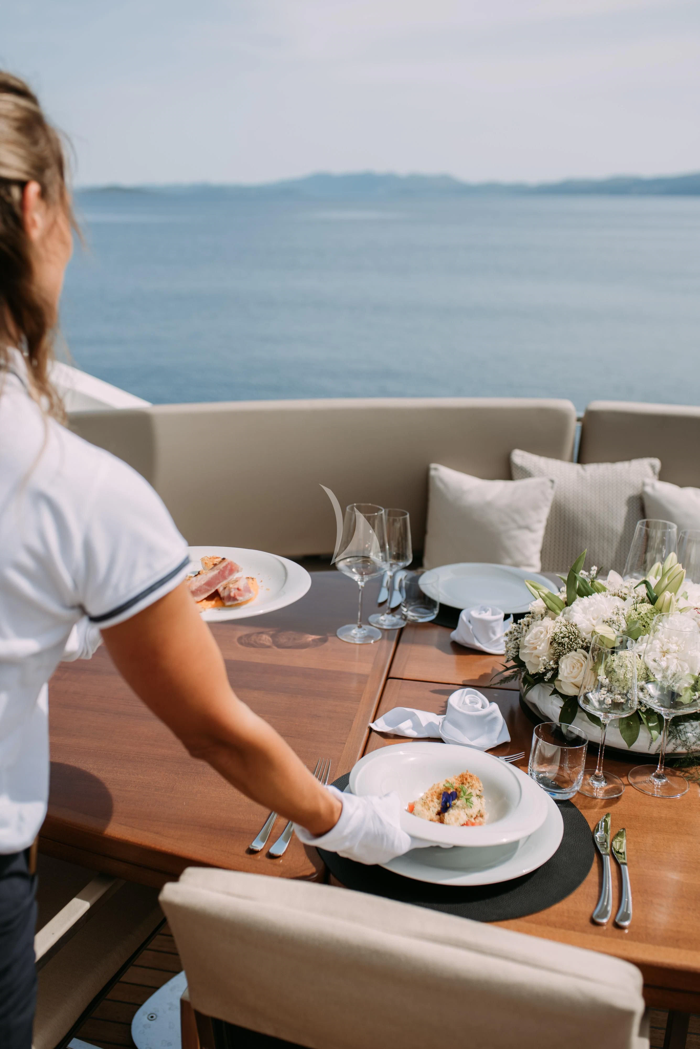 a woman sitting at a table with a plate of food and wine glasses aboard ARTEMY Yacht for Sale