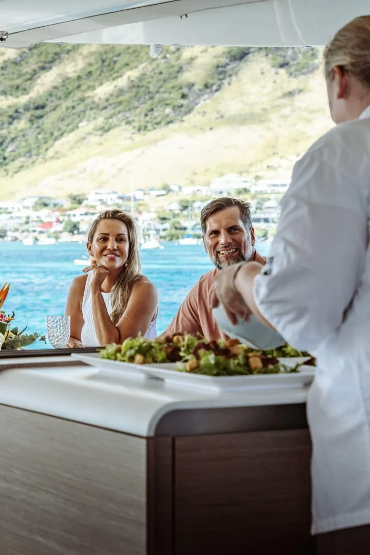 a man and woman standing at a table with a woman holding a plate of food aboard OCEANUS Yacht for Sale