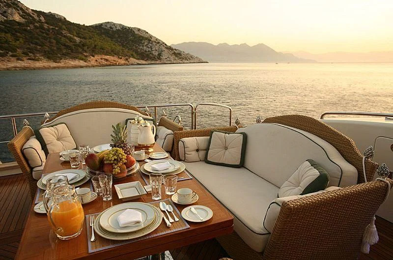 a table with chairs and a couch on it by a body of water aboard ALFA XII Yacht for Sale