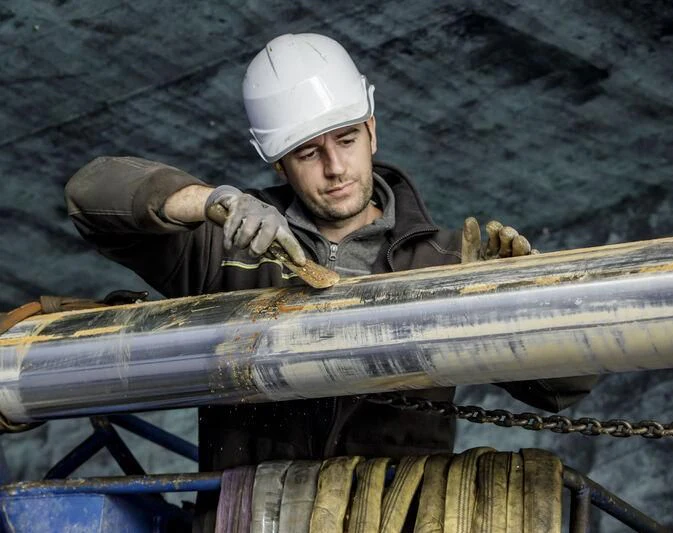 a person in a hardhat holding a large wooden pipe aboard OKTO Yacht for Charter