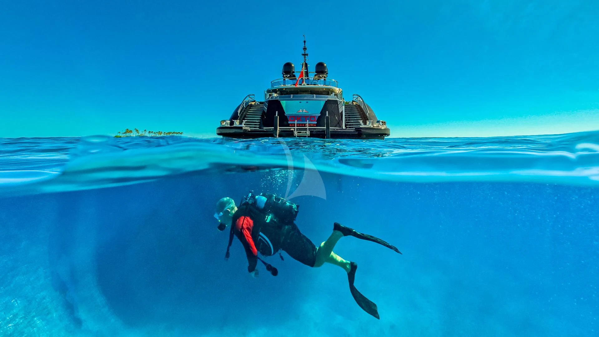 a group of people in scuba gear in the ocean with a boat in the background aboard OKTO Yacht for Charter