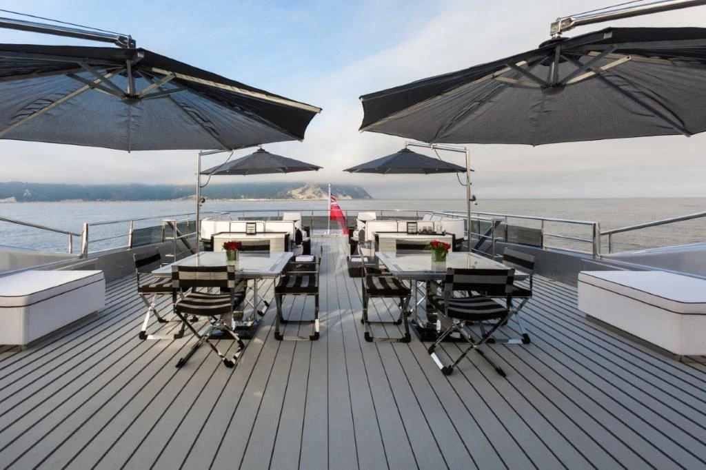 a deck with tables and chairs on it aboard OKTO Yacht for Charter