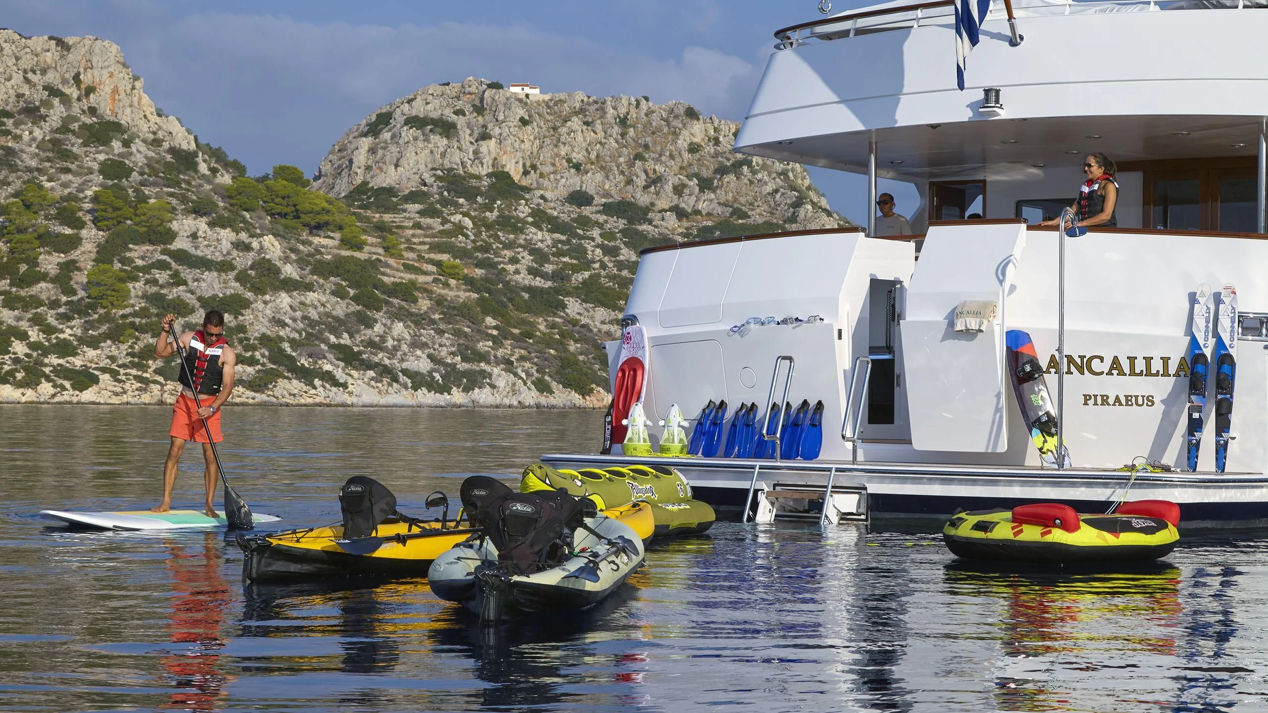 a person on a boat with a paddle and a couple of boats on the water aboard ANCALLIA Yacht for Sale