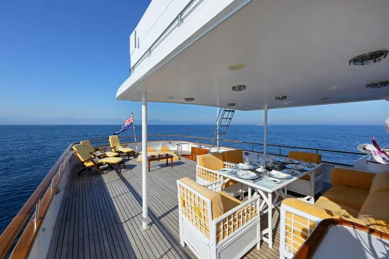 a deck with a table and chairs on it aboard RA Yacht for Sale