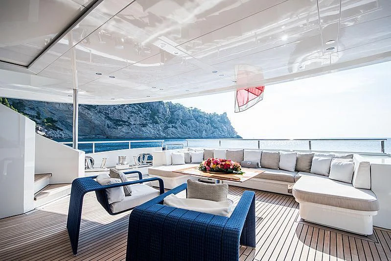 a room with a couch and a table with chairs and a large body of water in the background aboard ZIA Yacht for Sale