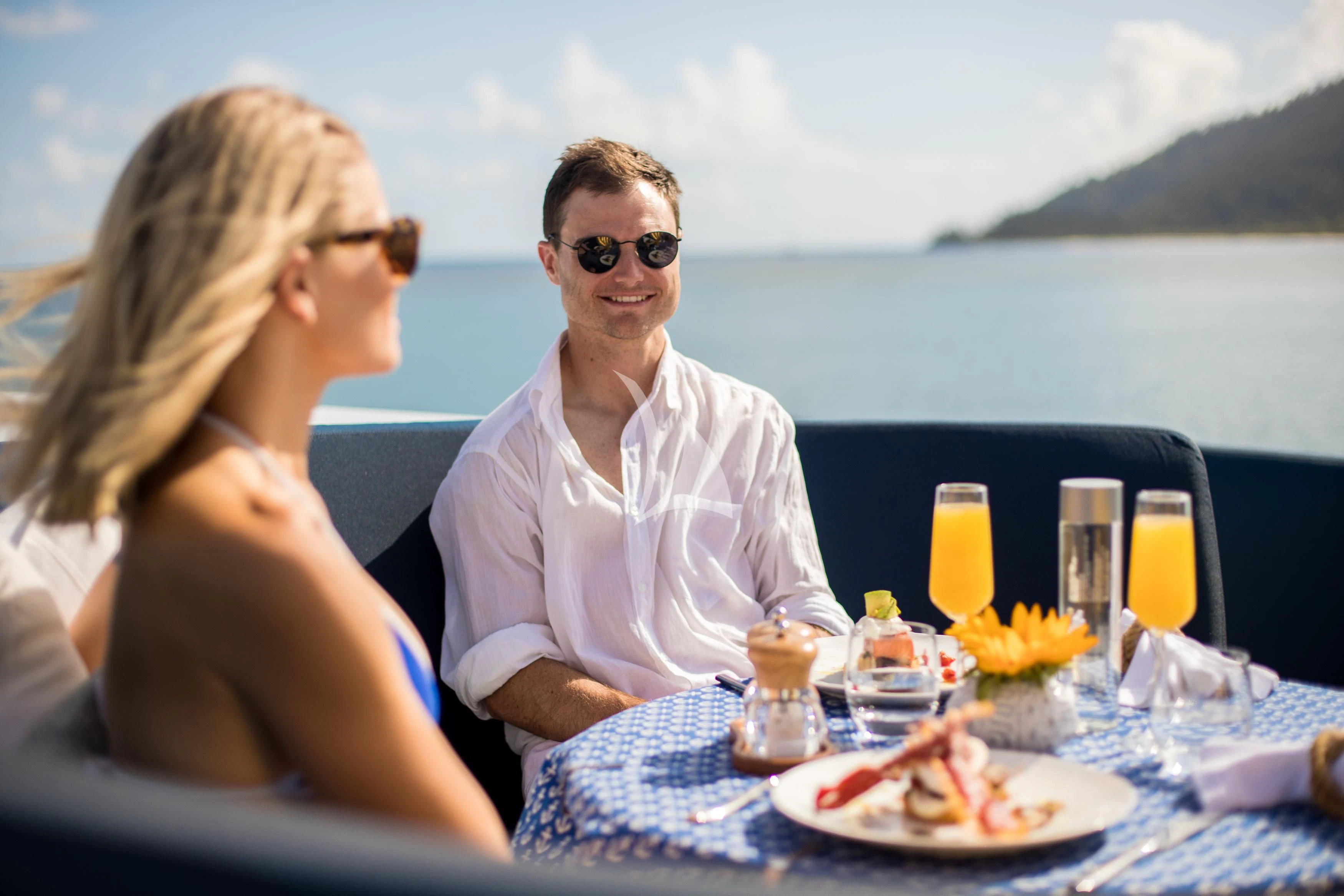 a man and woman sitting at a table with food and drinks on it aboard DE LISLE III Yacht for Sale