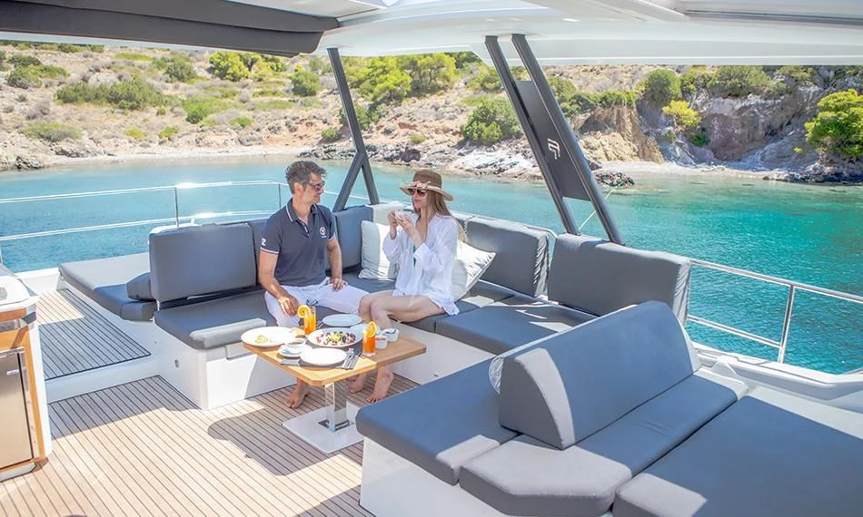 a man and woman sitting at a table on a deck with a view of a lake and mountains aboard PRINCESS MILA Yacht for Charter