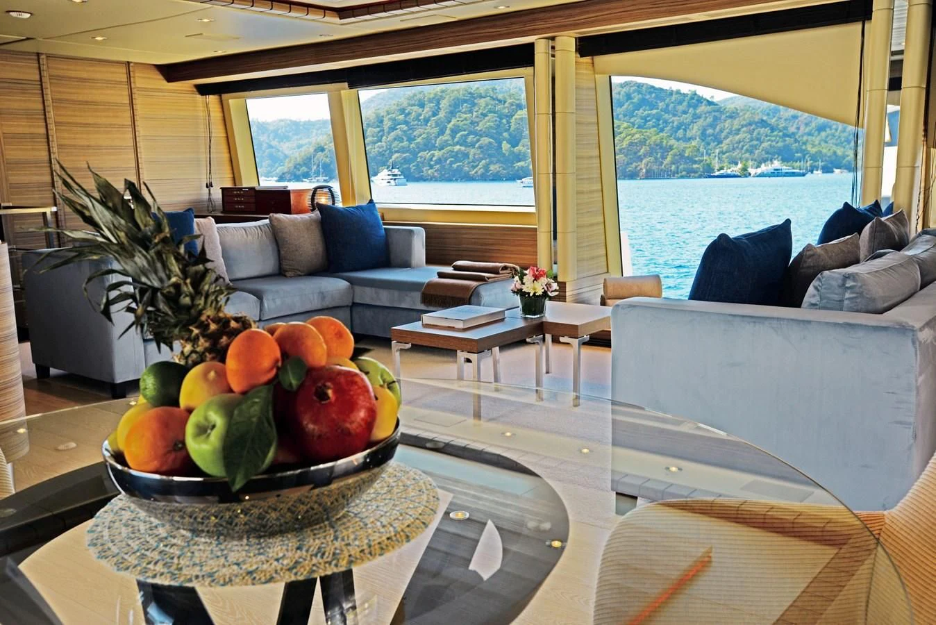 a large living room with a large window and a large table with fruit on it aboard ORYX Yacht for Sale