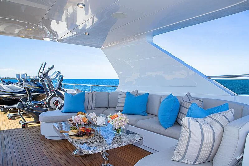a white lounge chair next to a white couch with blue pillows and a white table with a blue aboard AMORE Yacht for Charter