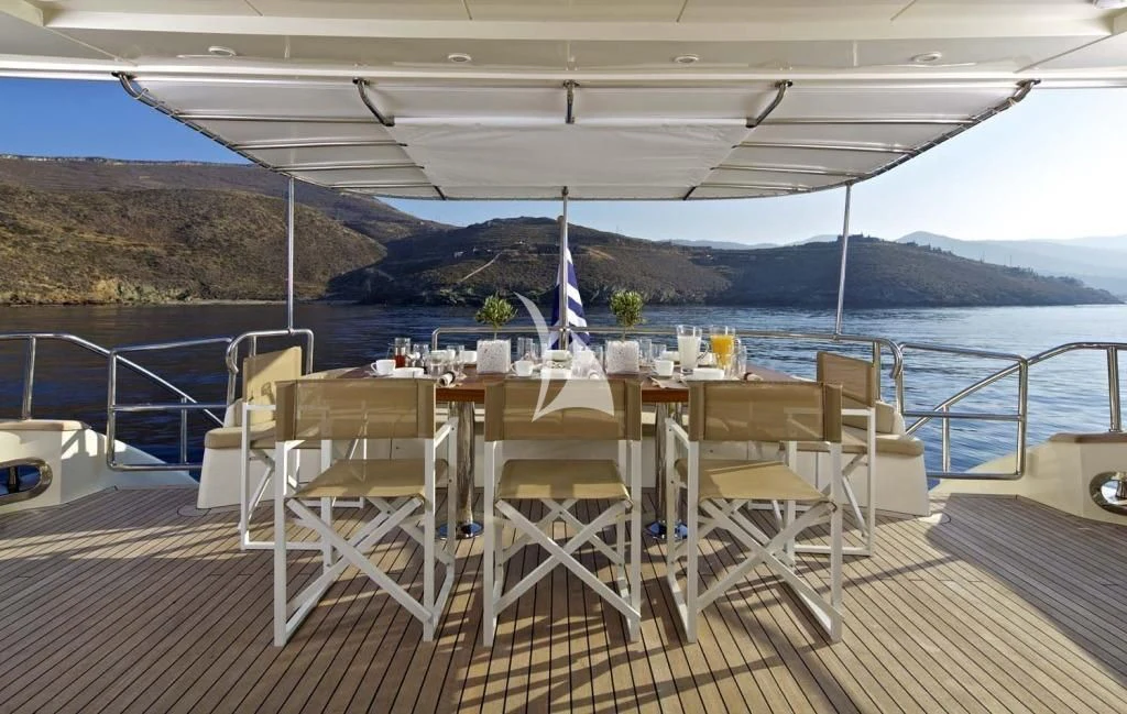 a deck with tables and chairs on it and water in the background aboard SANJANA Yacht for Sale