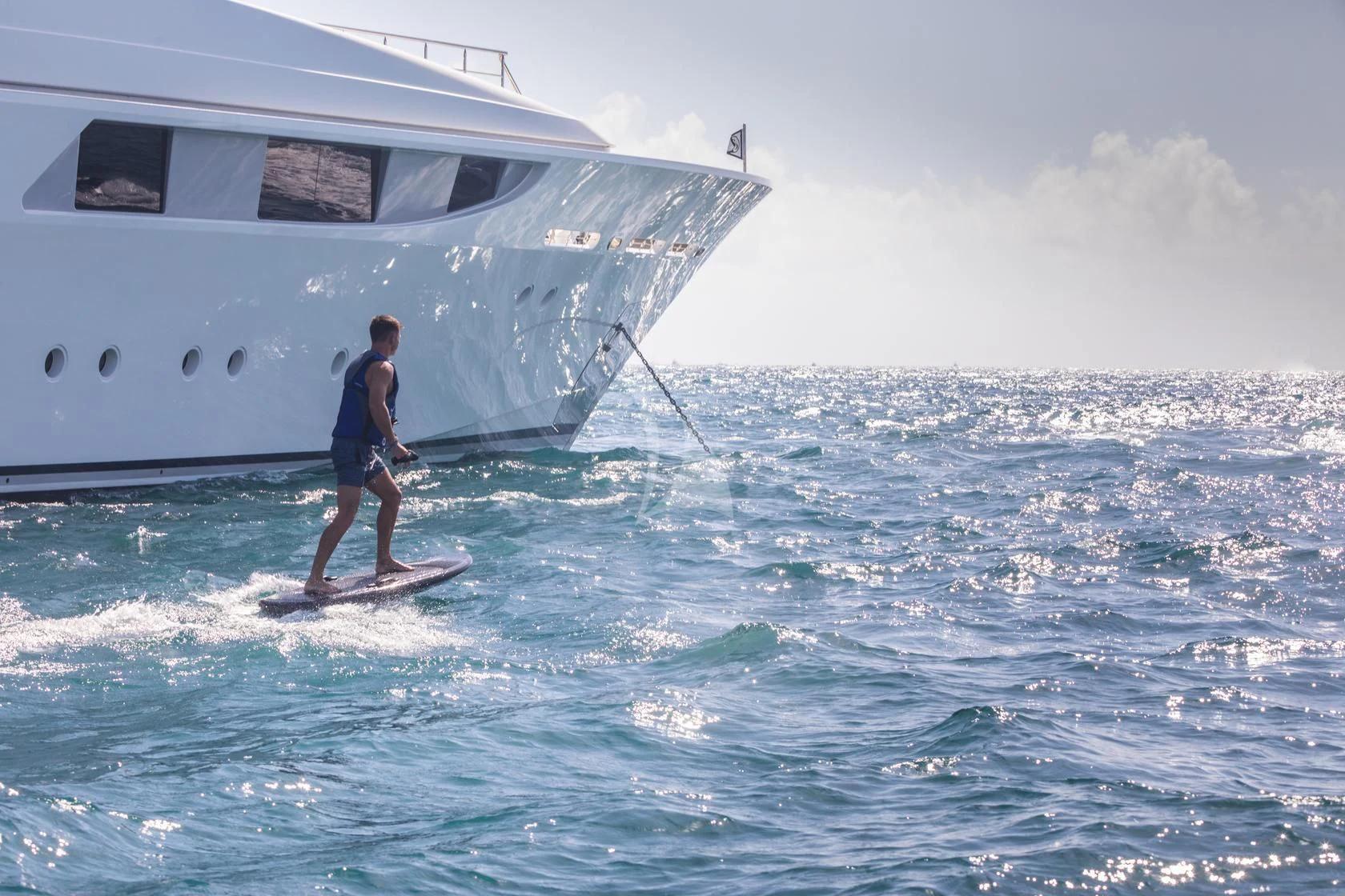 a man on a surfboard in the ocean next to a boat aboard CHASING DAYLIGHT Yacht for Sale