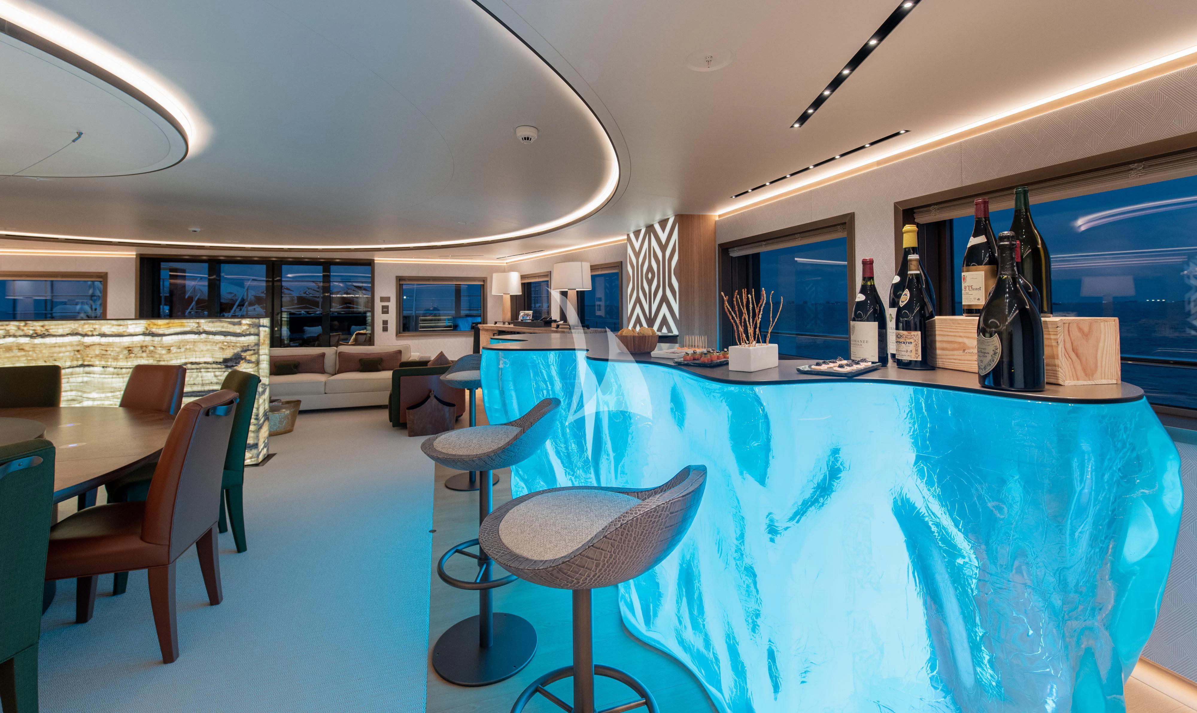 a large room with a table and chairs and bottles on the table aboard LA DATCHA Yacht for Sale