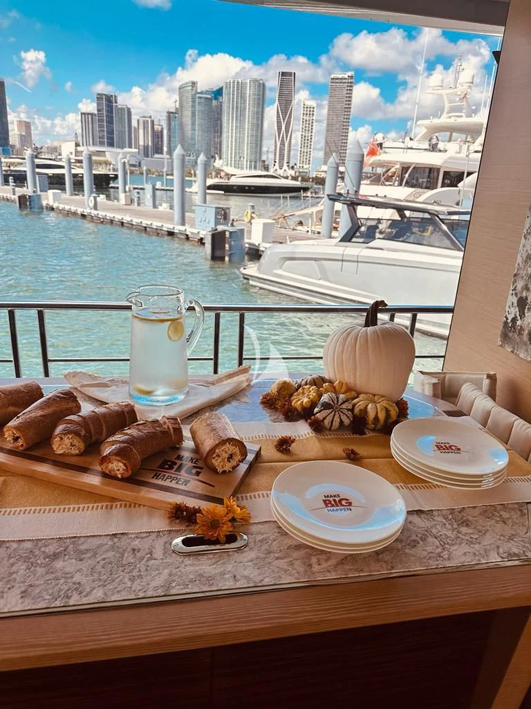 a table with food and drinks on it by a window with a city in the background aboard MAKE BIG HAPPEN Yacht for Sale