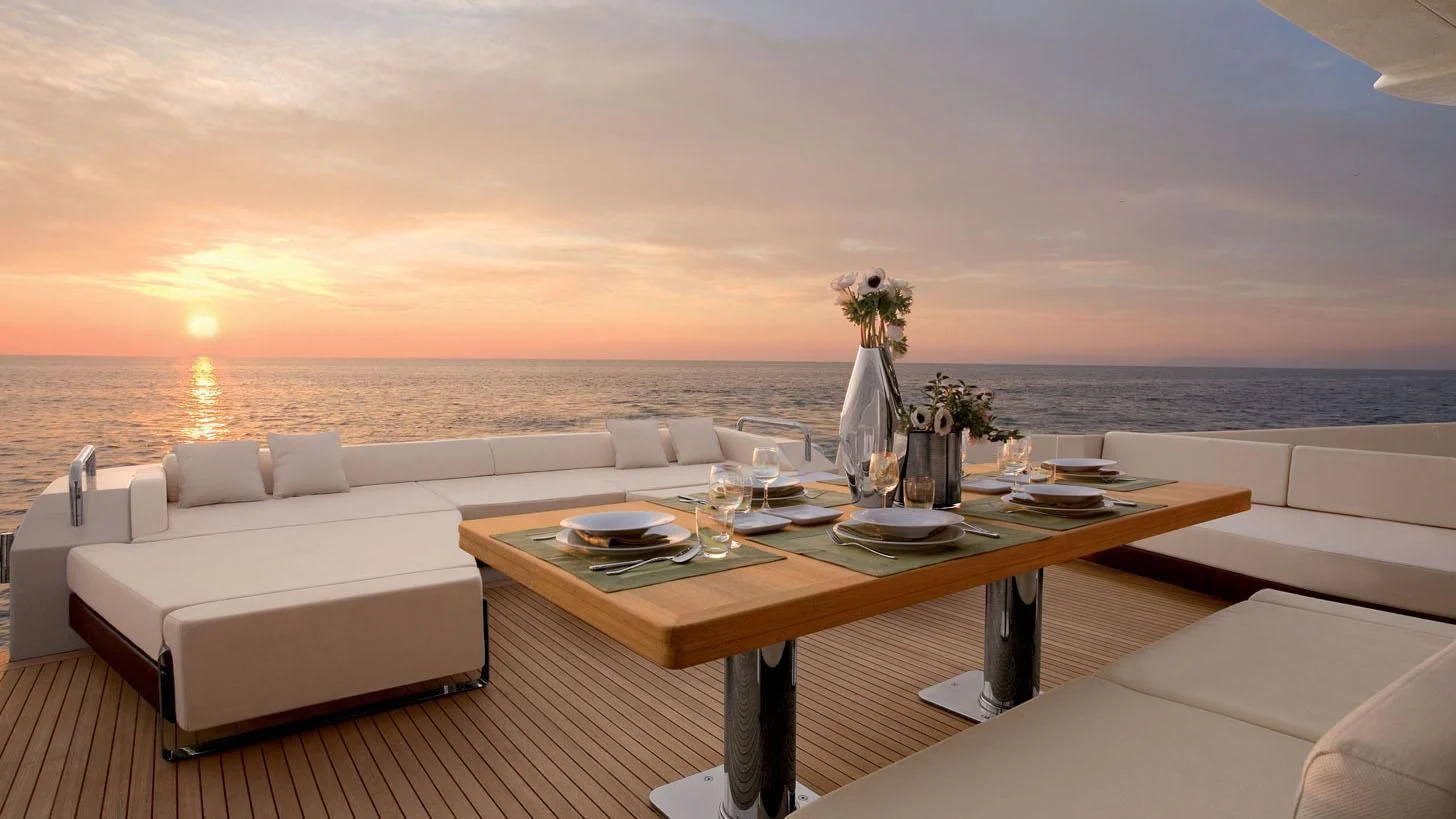 a table with chairs and a couch on a balcony overlooking a sunset aboard DUKE Yacht for Sale