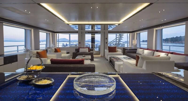 a living room with a large blue table and white couches aboard KAMALAYA Yacht for Sale