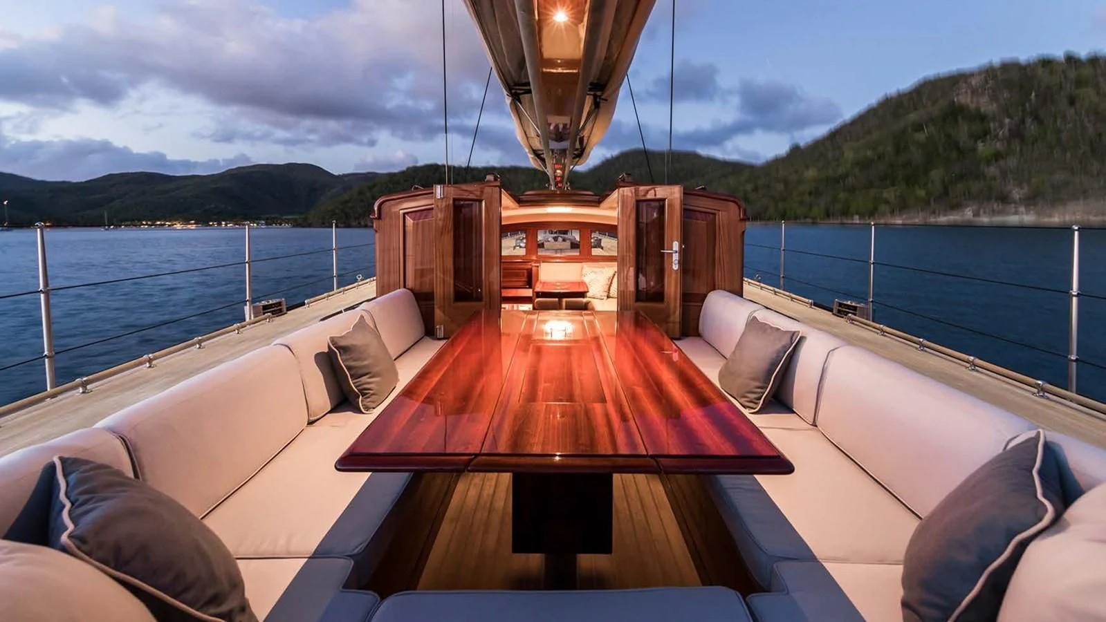 a deck with a wood table and a large body of water in the background aboard RAINBOW Yacht for Sale