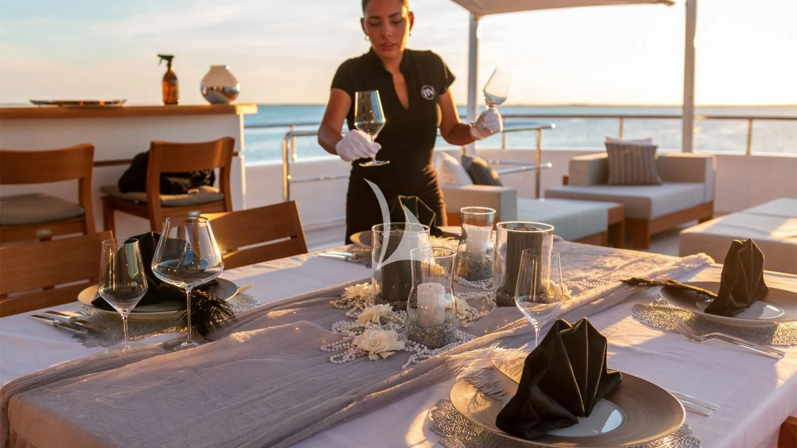 a person standing next to a table with glasses and a hat aboard BON VIVANT Yacht for Sale