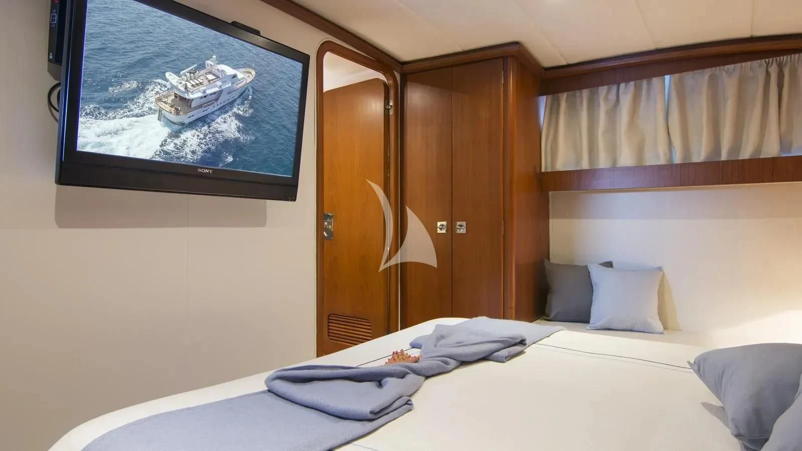 a bed with a white bed spread and a large television on the wall aboard OCEANE II Yacht for Sale