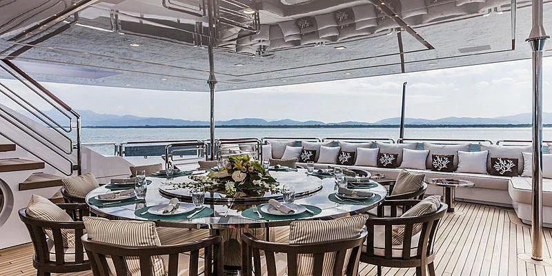 a table set for a meal on a patio with a large body of water in the background aboard PARILLION Yacht for Sale