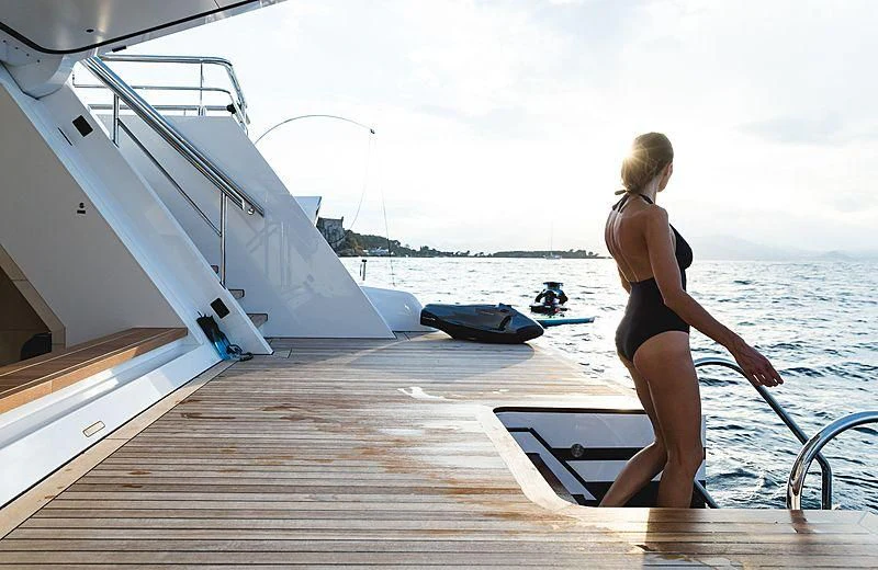 a person in a bikini walks on a dock with a surfboard aboard VOLPINI 2 Yacht for Sale