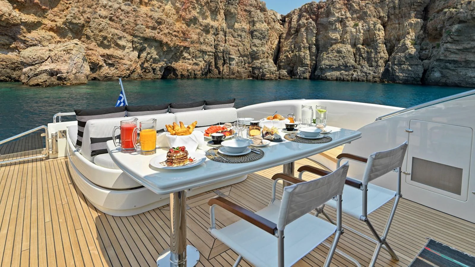 a table with food on it and chairs on a deck by a body of water aboard RUBY Yacht for Charter