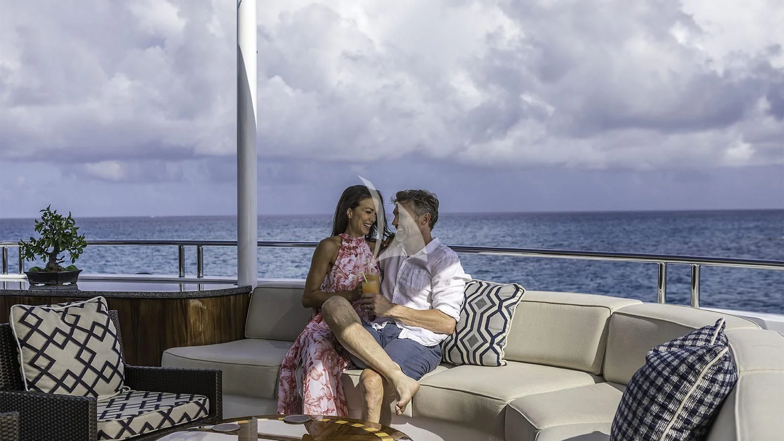 a man and woman sitting on a couch with a body of water in the background aboard LADY BETH Yacht for Sale