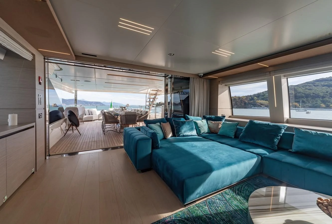 a large living room with a blue couch and a large window aboard FRANGELO Yacht for Sale