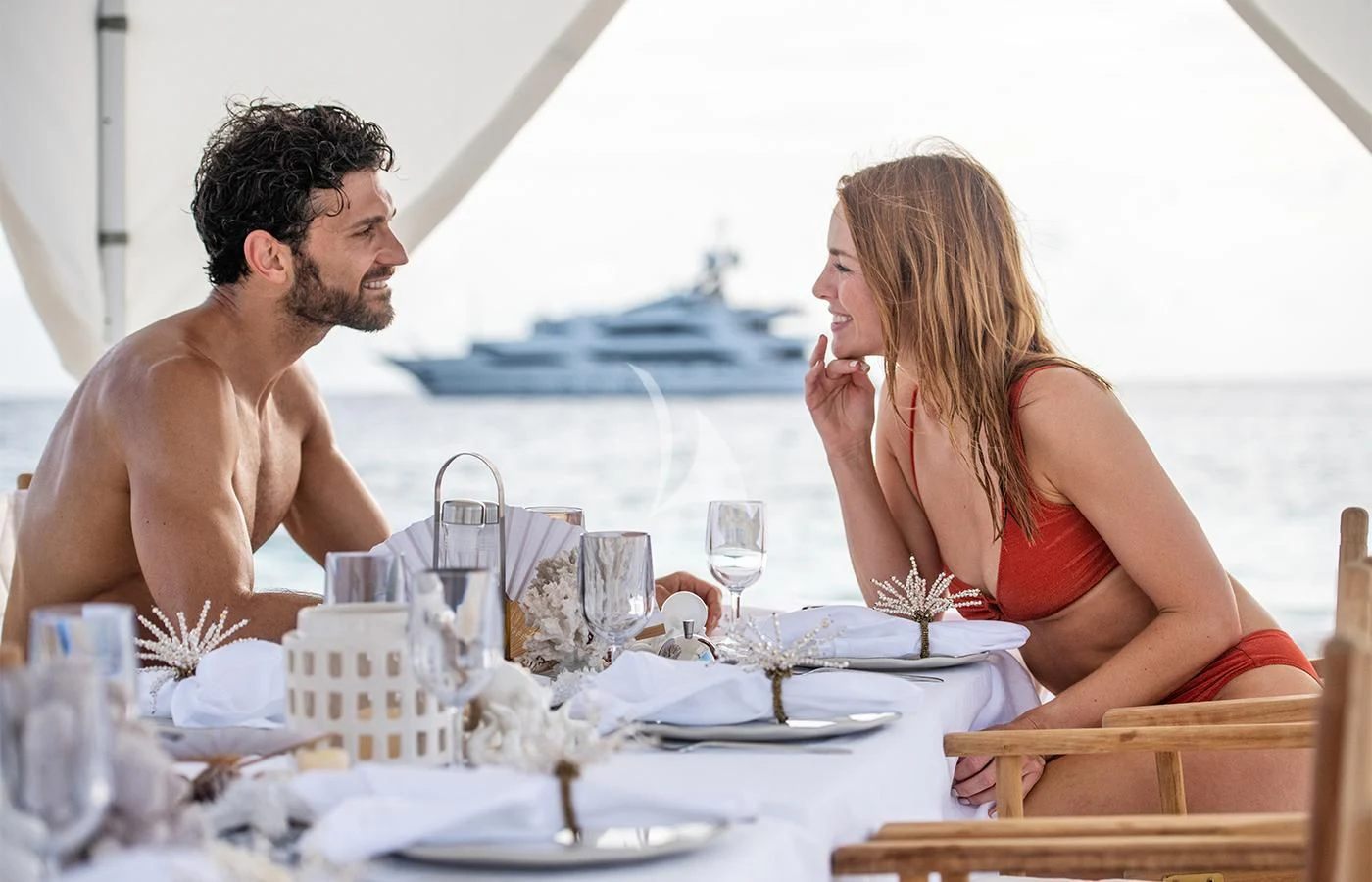 a man and woman sitting at a table with a white tablecloth and chairs with a white tent aboard JAGUAR Yacht for Charter