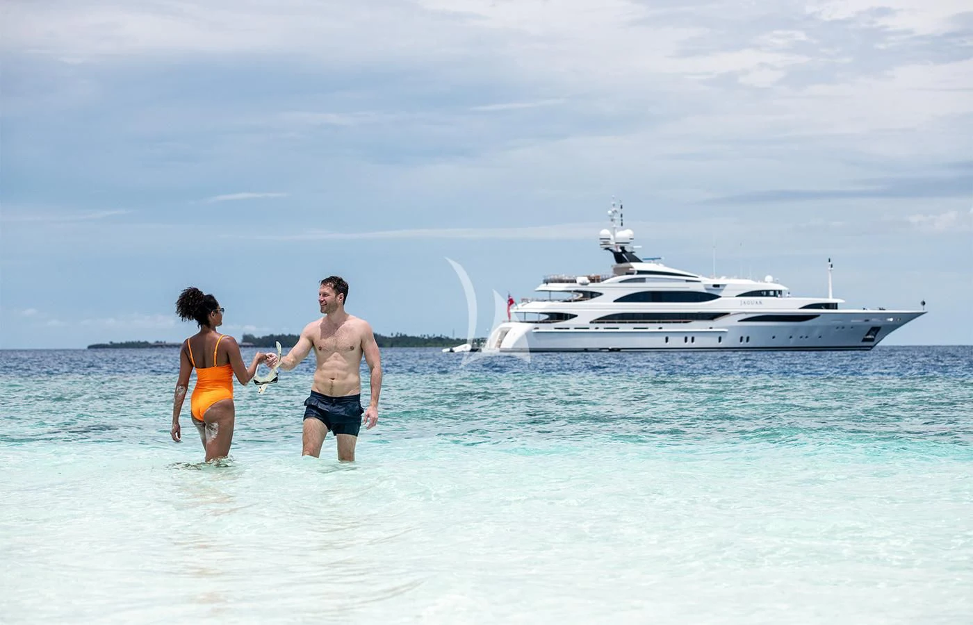 a man and woman walking into the water with a boat in the background aboard JAGUAR Yacht for Charter