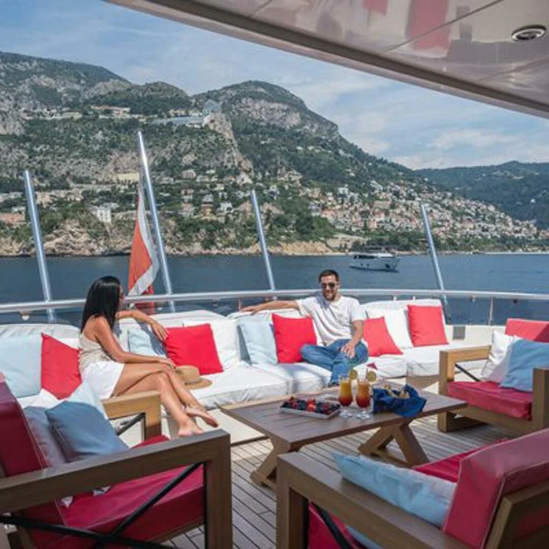 people sitting on lounge chairs on a beach with a sailboat in the background aboard IRAMA Yacht for Sale