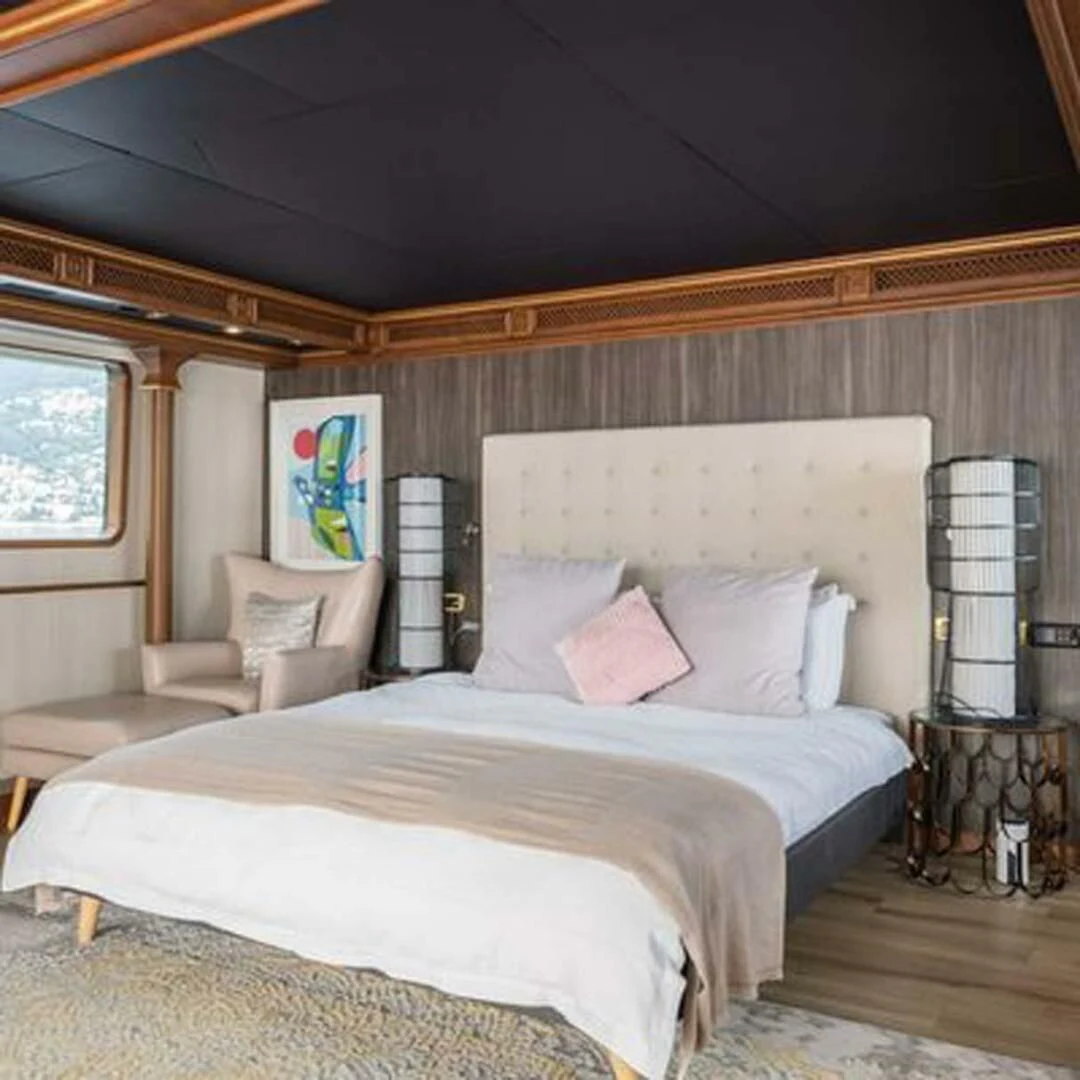 a bed with a white sheet and pillows in a room with a window aboard IRAMA Yacht for Sale