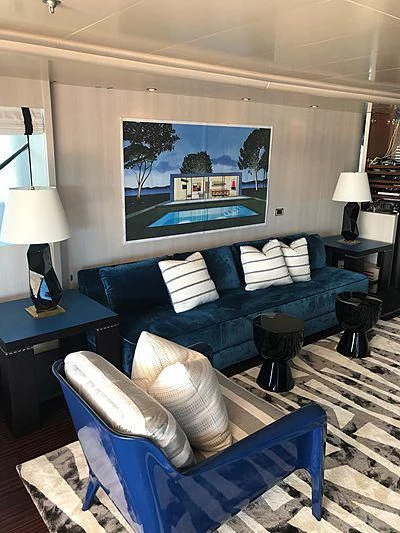 a living room with a large blue couch and a large painting aboard ETERNITY Yacht for Sale