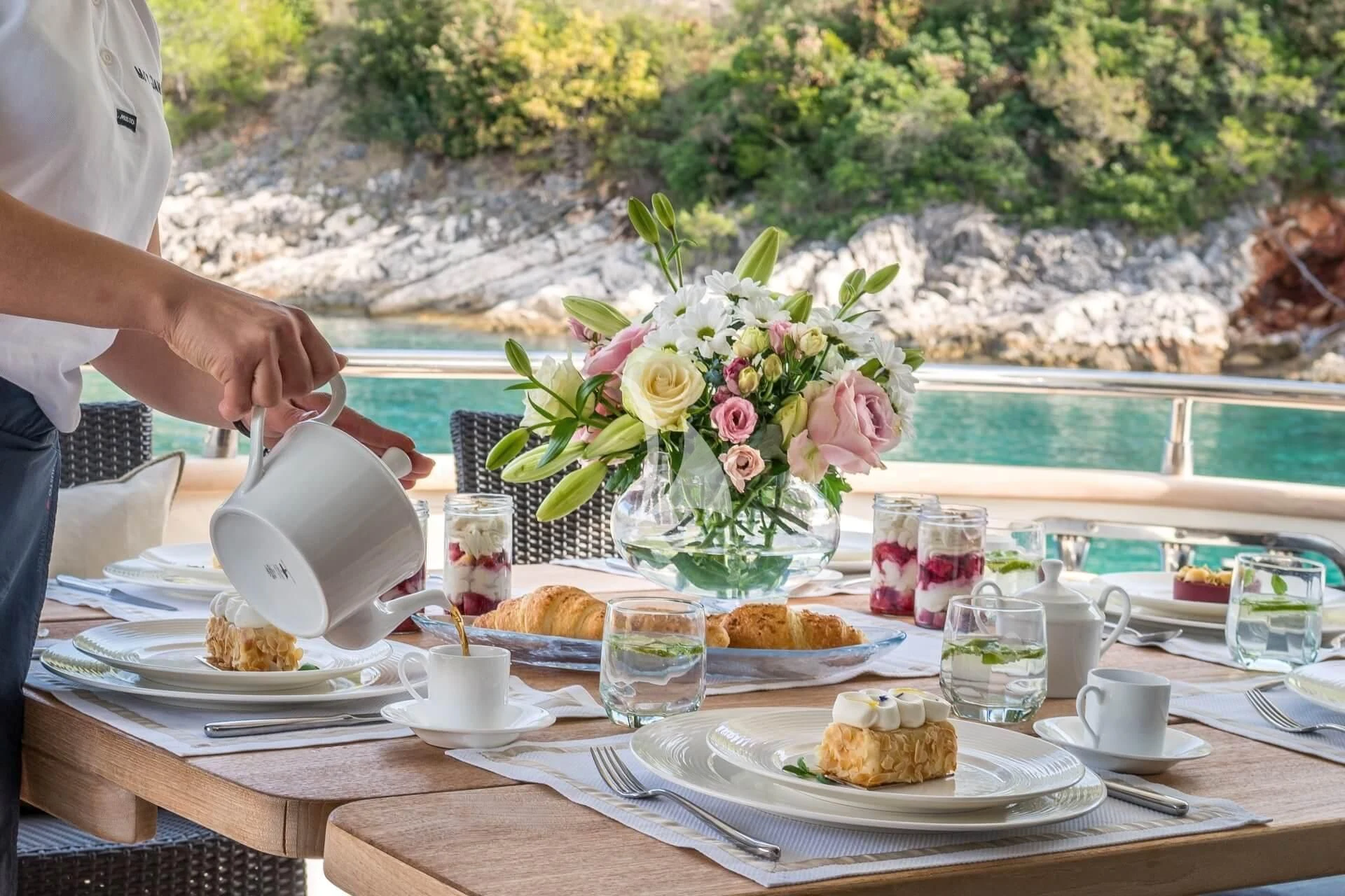 a person pouring a drink into a cup on a table aboard JANTAR Yacht for Charter
