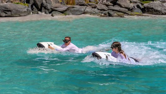 a man and woman riding a surfboard in the ocean aboard SCOTT FREE Yacht for Charter