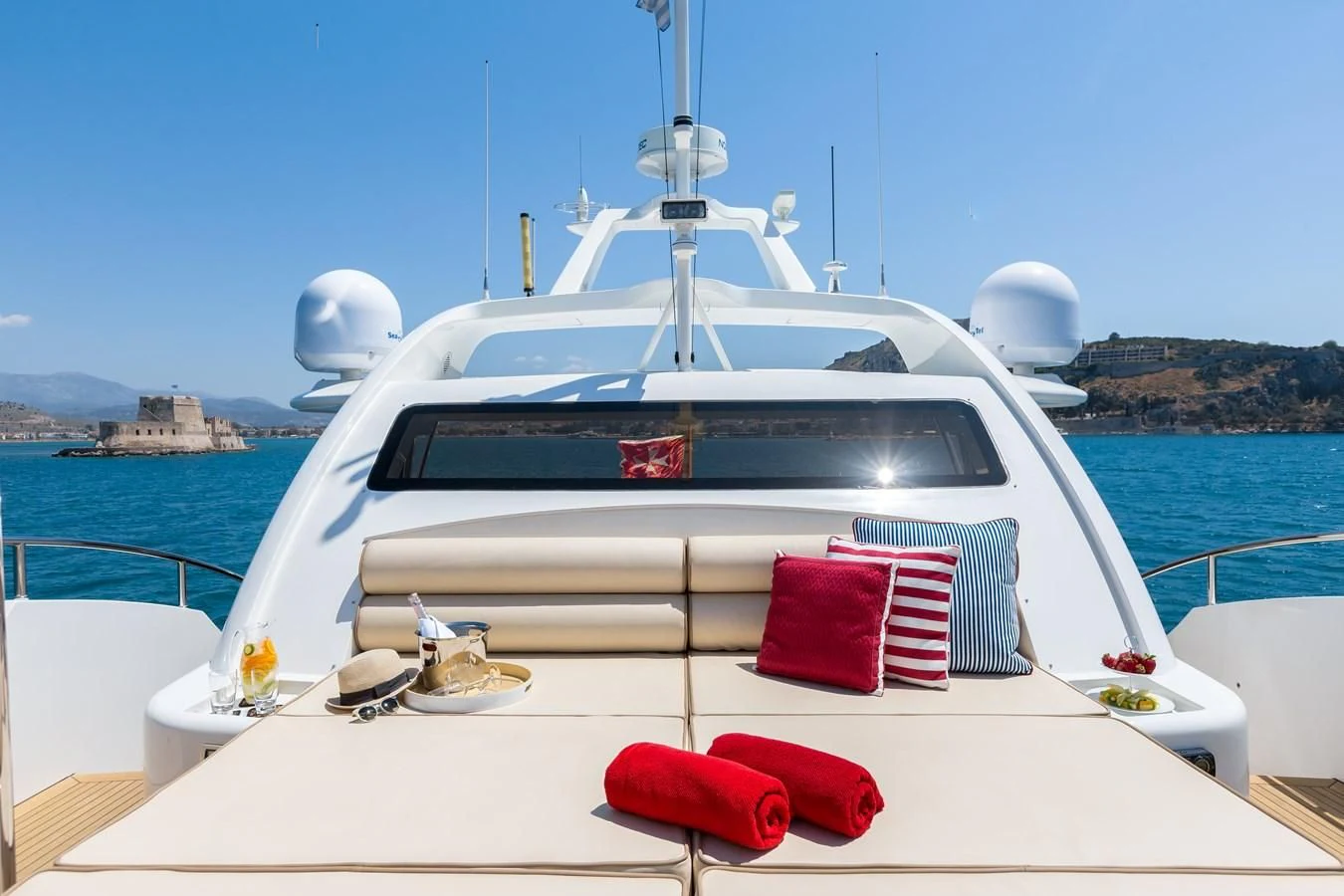 a white boat with red pillows on a white surface with a red towel on it aboard REBECCA V Yacht for Sale