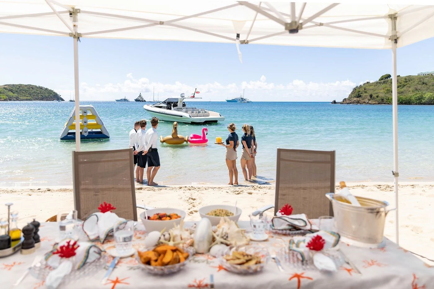 a group of people standing on a beach with food and a boat in the background aboard GLADIATOR Yacht for Sale