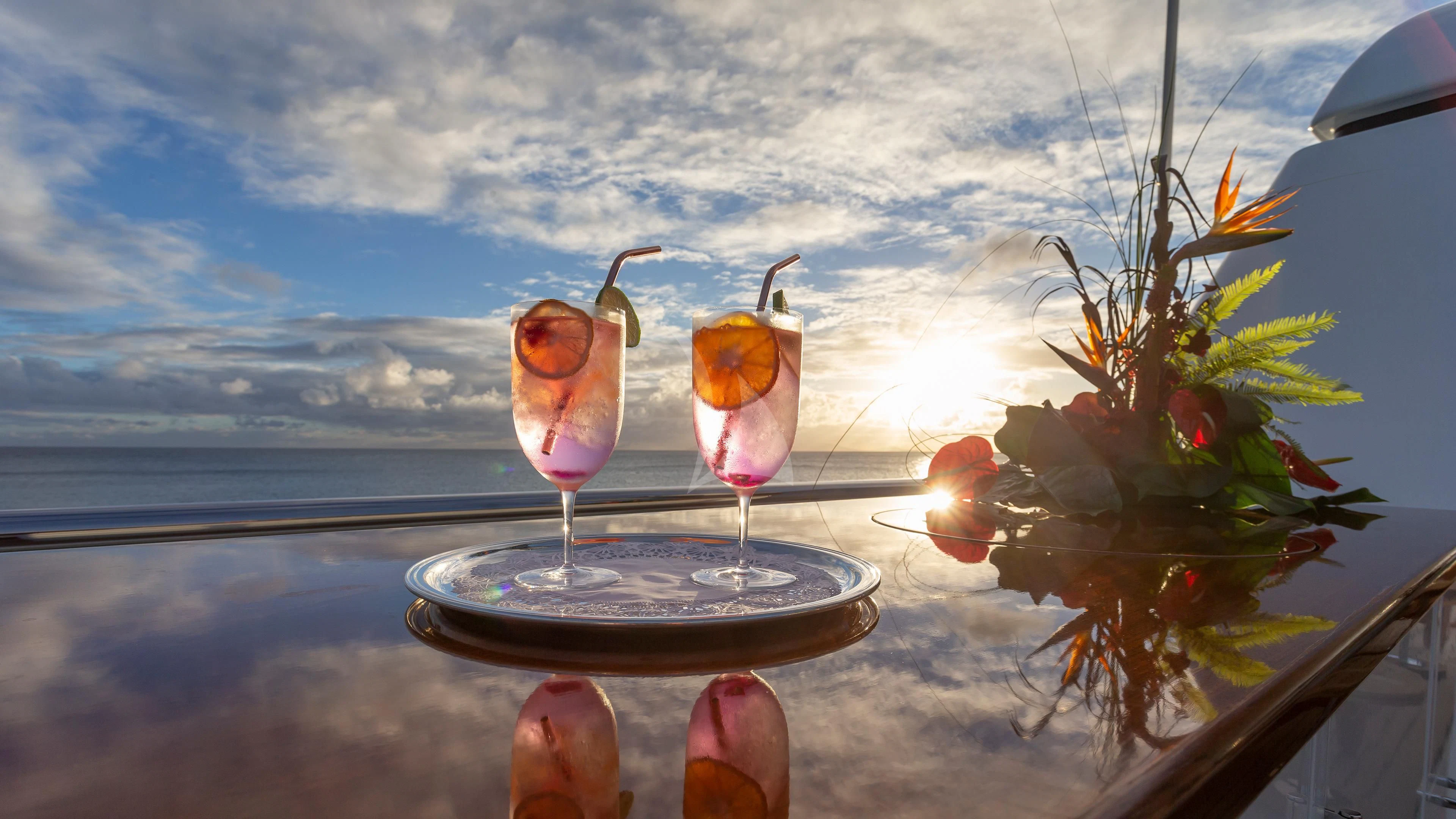 a group of glasses with drinks on a table with a view of the ocean and a city in aboard GLADIATOR Yacht for Sale