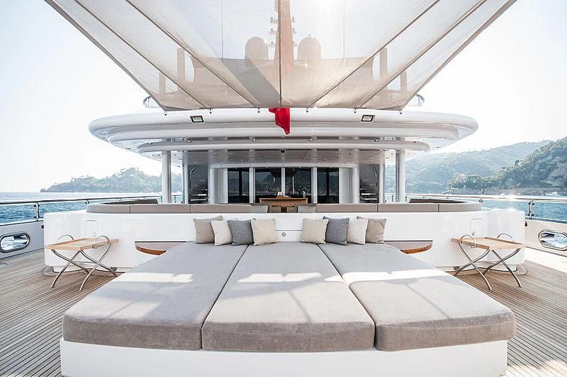 a large white lounge chair on a deck with a large white boat in the background aboard TRIPLE SEVEN Yacht for Sale