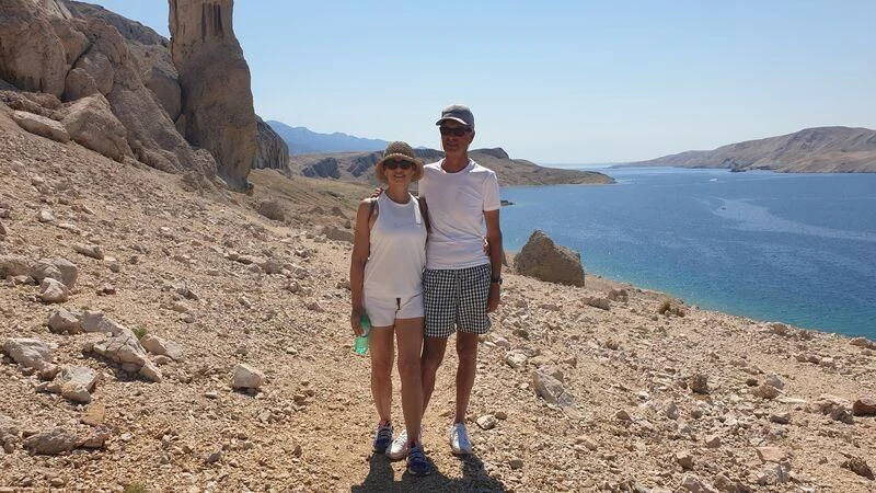a man and woman standing on a rocky hill overlooking a body of water aboard MIAMAA Yacht for Sale