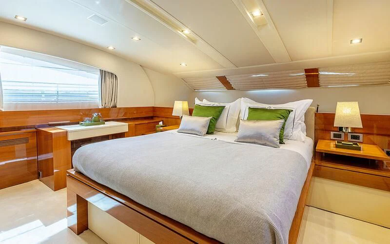 a bed with a white comforter and pillows in a room with a window and a desk with aboard APMONIA Yacht for Sale